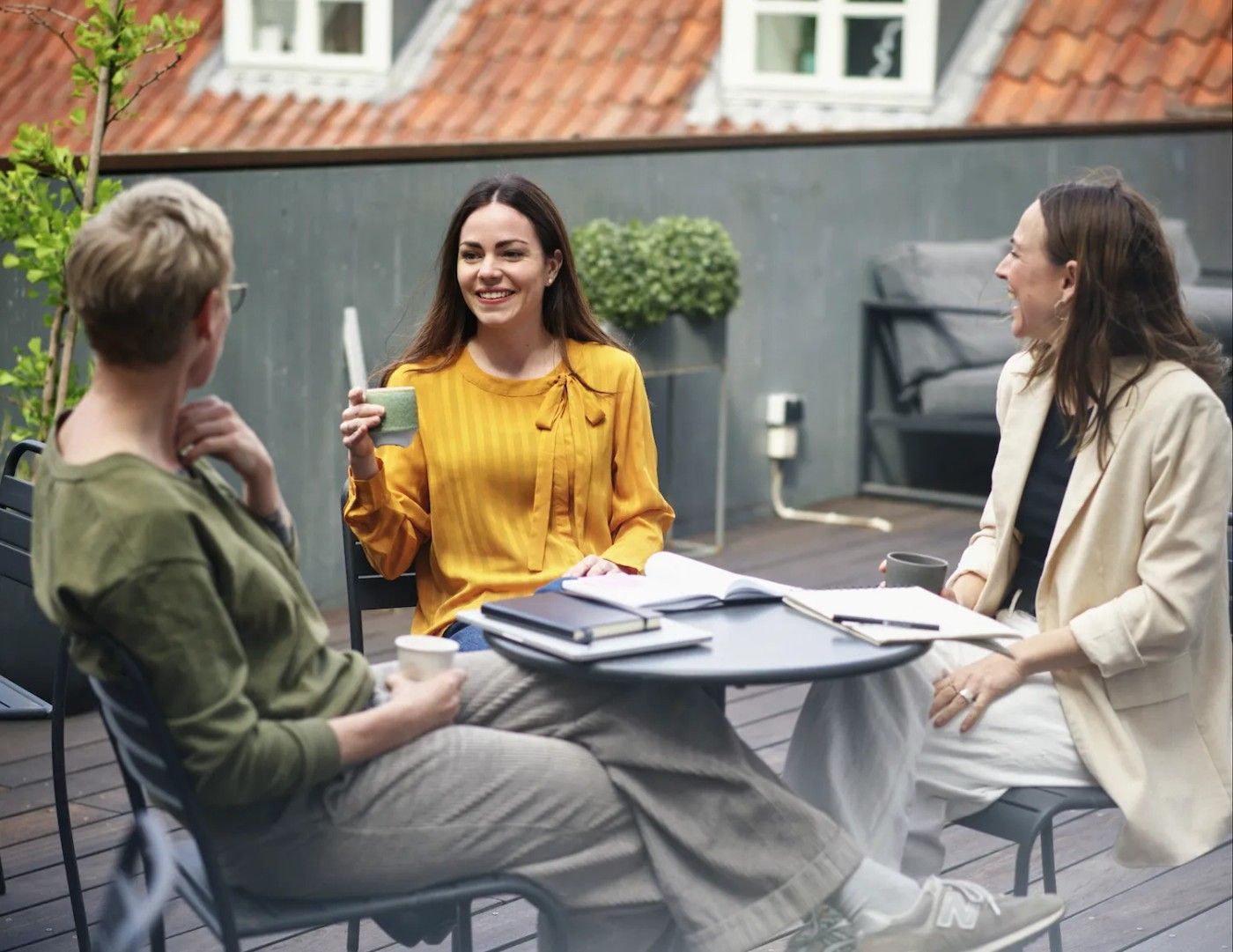 Three colleagues talking over coffee and notebooks at a table on a roof terrace